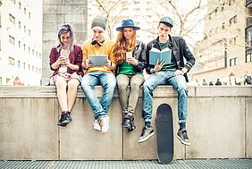 vier junge Menschen sitzen auf einer Mauer