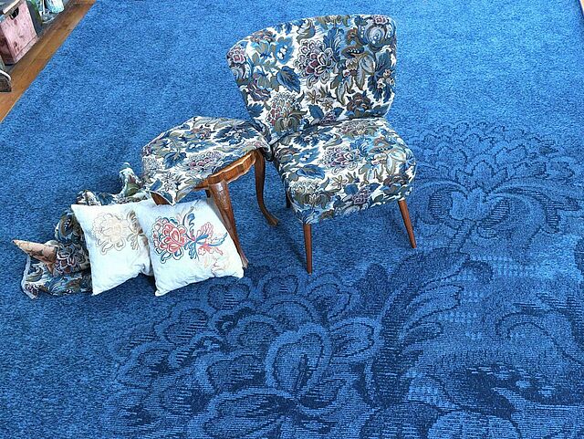 Sessel und Hocker auf einem blauen Teppich stehend.