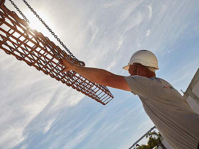 Ein Bauarbeiter hält ein Eisengitter.