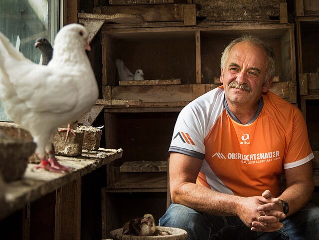Ein Mann sitzt mit einer weißen Taube im Taubenschlag.
